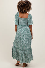 woman wearing a green floral maternity maxi dress with flutter sleeves and a tiered skirt, showing her back