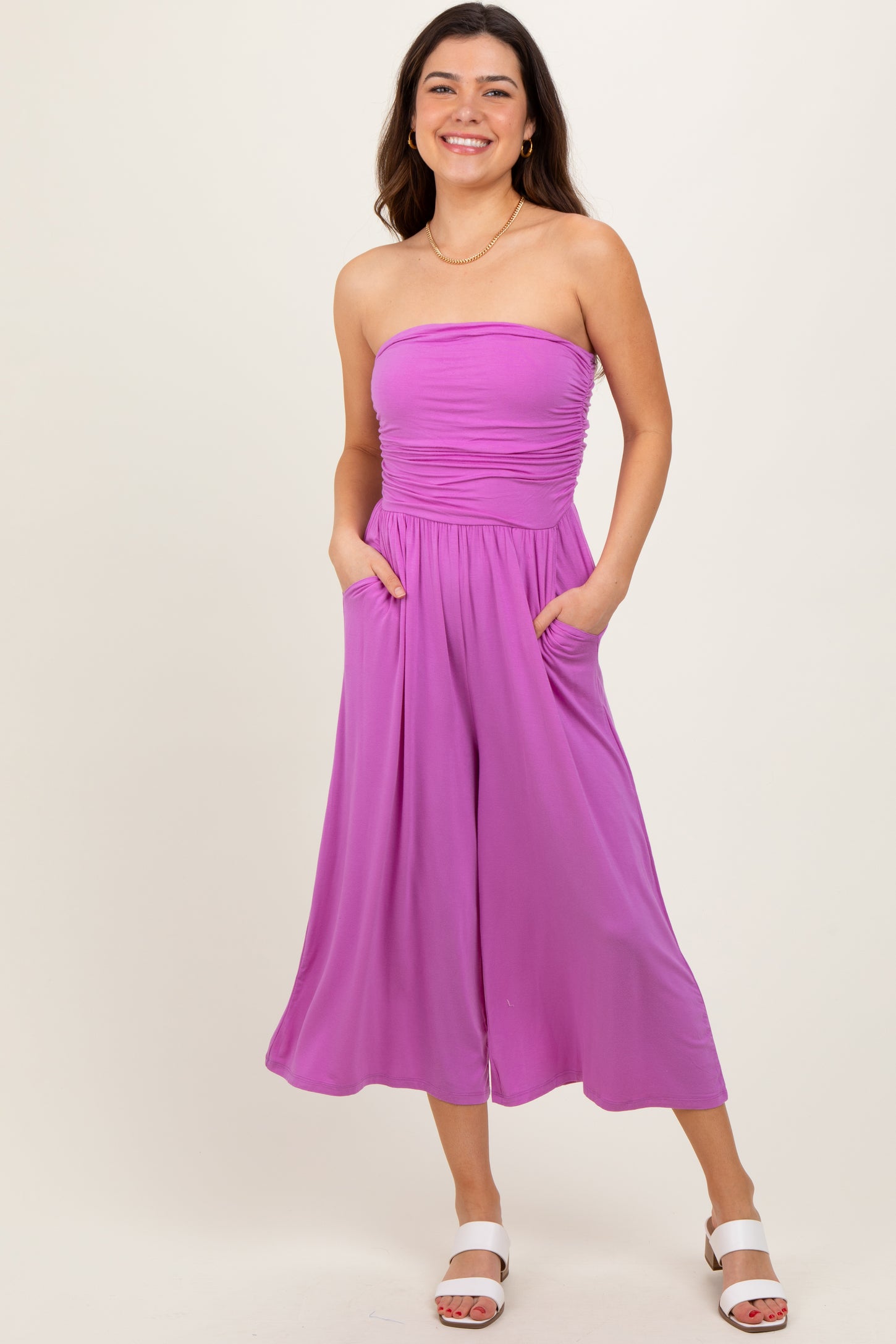 woman wearing a strapless purple jumpsuit with wide legs and pockets, smiling at the camera
