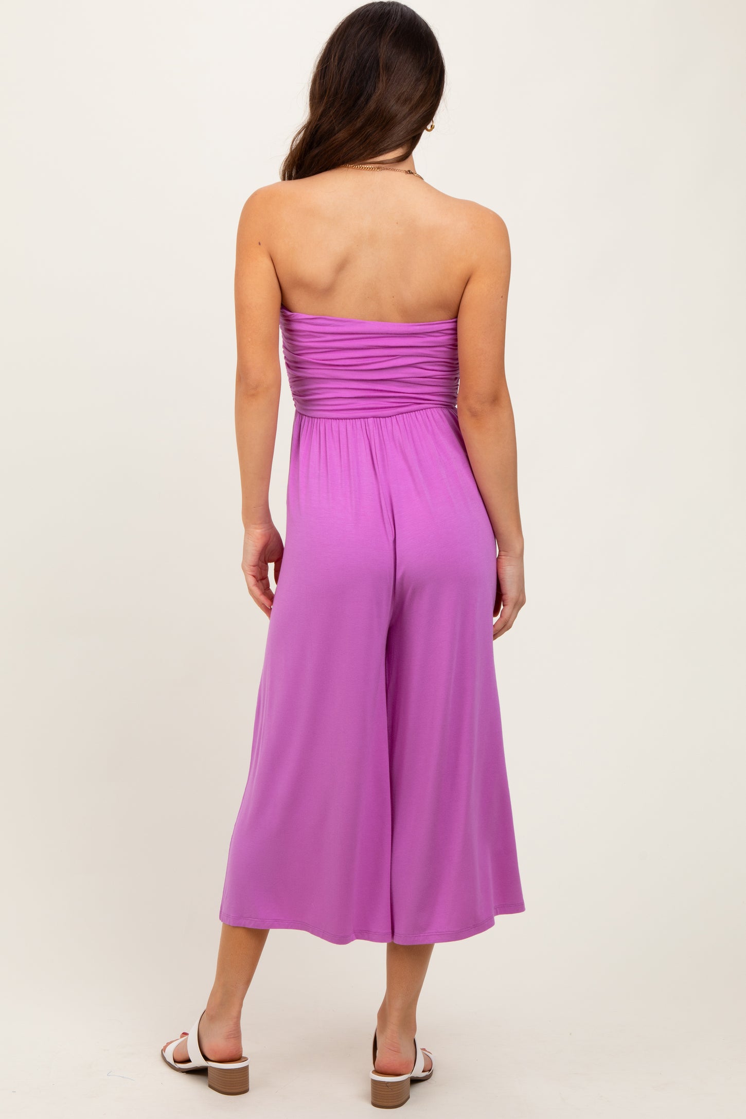 woman wearing a solid pink strapless jumpsuit with a gathered bodice and wide-leg trousers, shown from the back