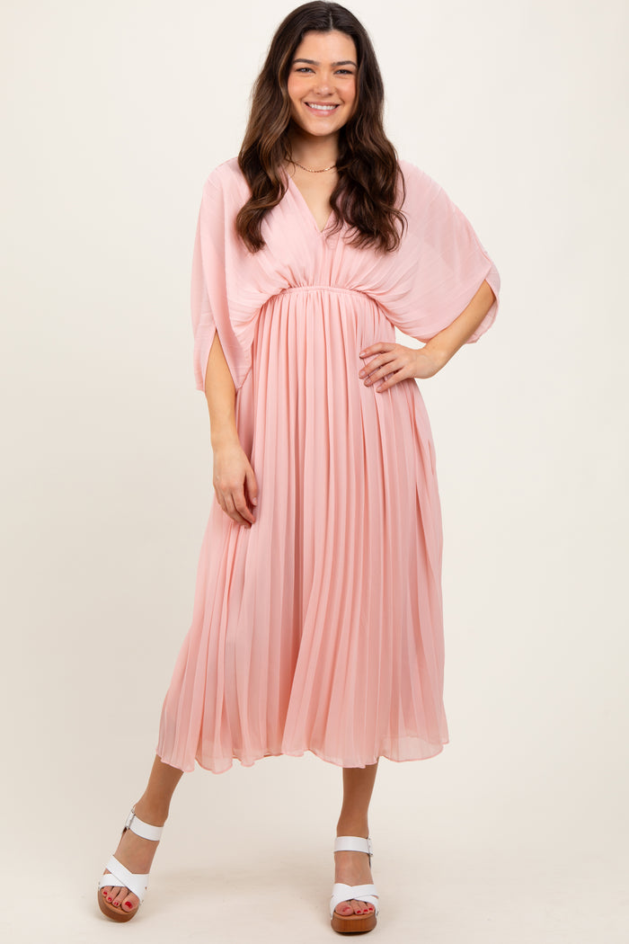 woman wearing a light pink pleated midi dress with a flowy cape sleeve and a cinched waist