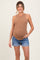 woman wearing a light brown ribbed maternity tank top and denim shorts, showing her baby bump