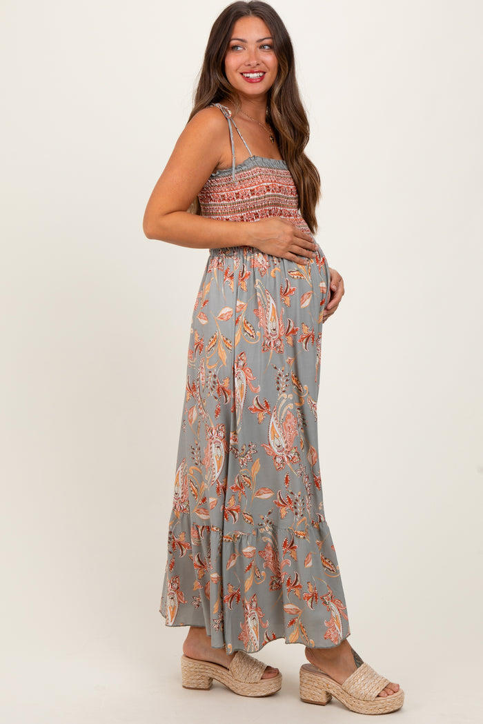 woman wearing a grey floral maternity maxi dress with a smocked bodice and holding her baby bump