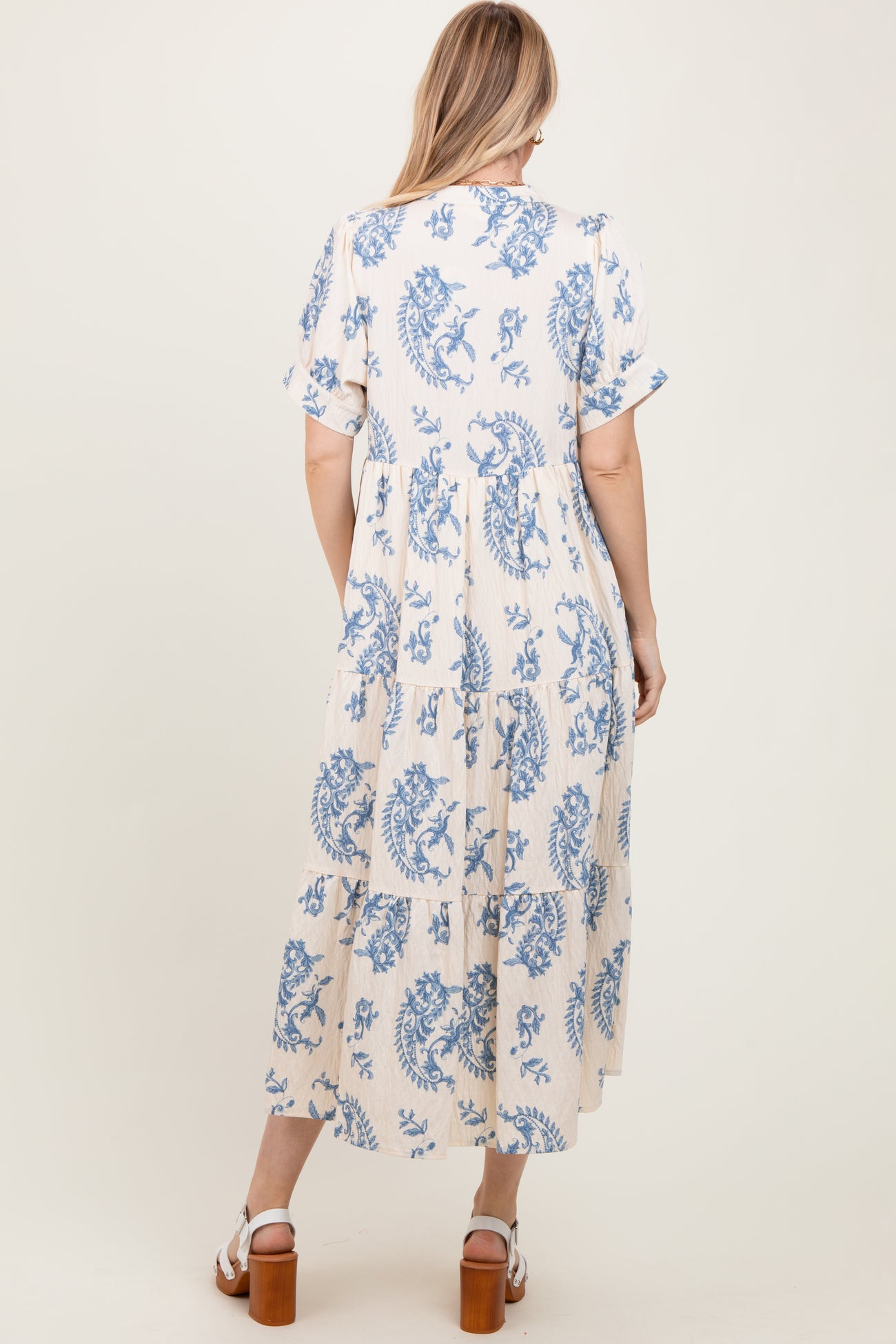 woman wearing a beige maxi dress with blue floral print and short sleeves, showing the back view