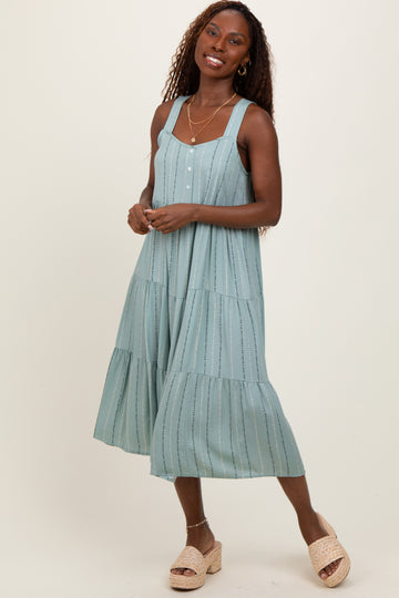 woman wearing a light blue midi dress with tiered ruffle details and buttons, standing in a relaxed pose