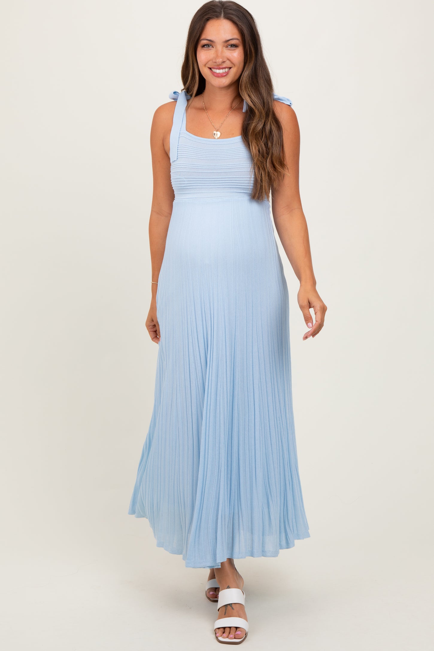 woman wearing a light blue maternity maxi dress with tie strap details and flowing pleats