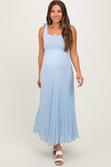 woman wearing a light blue maternity maxi dress with tie strap details and flowing pleats