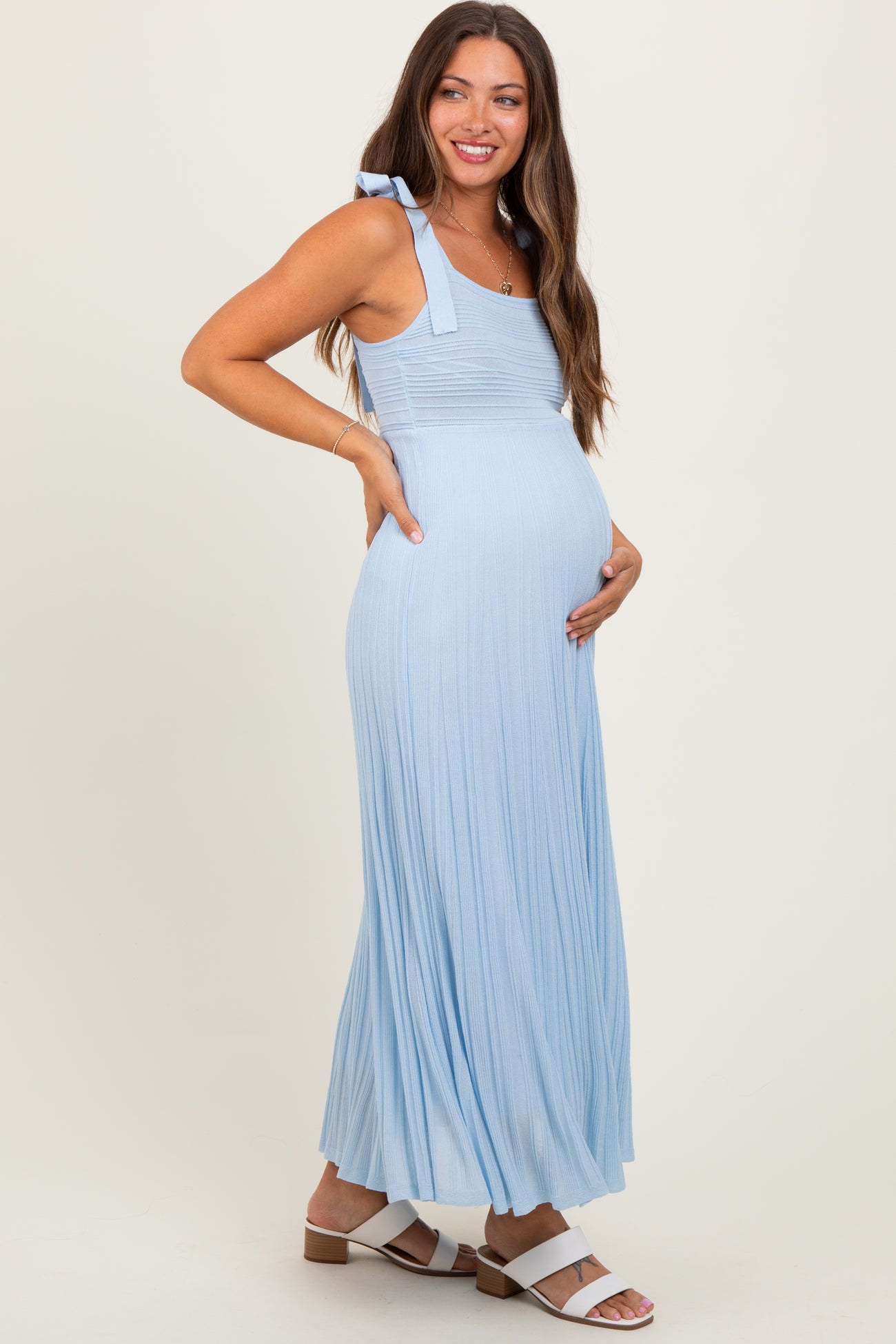 woman wearing a light blue maternity maxi dress with tie shoulder straps and holding her baby bump