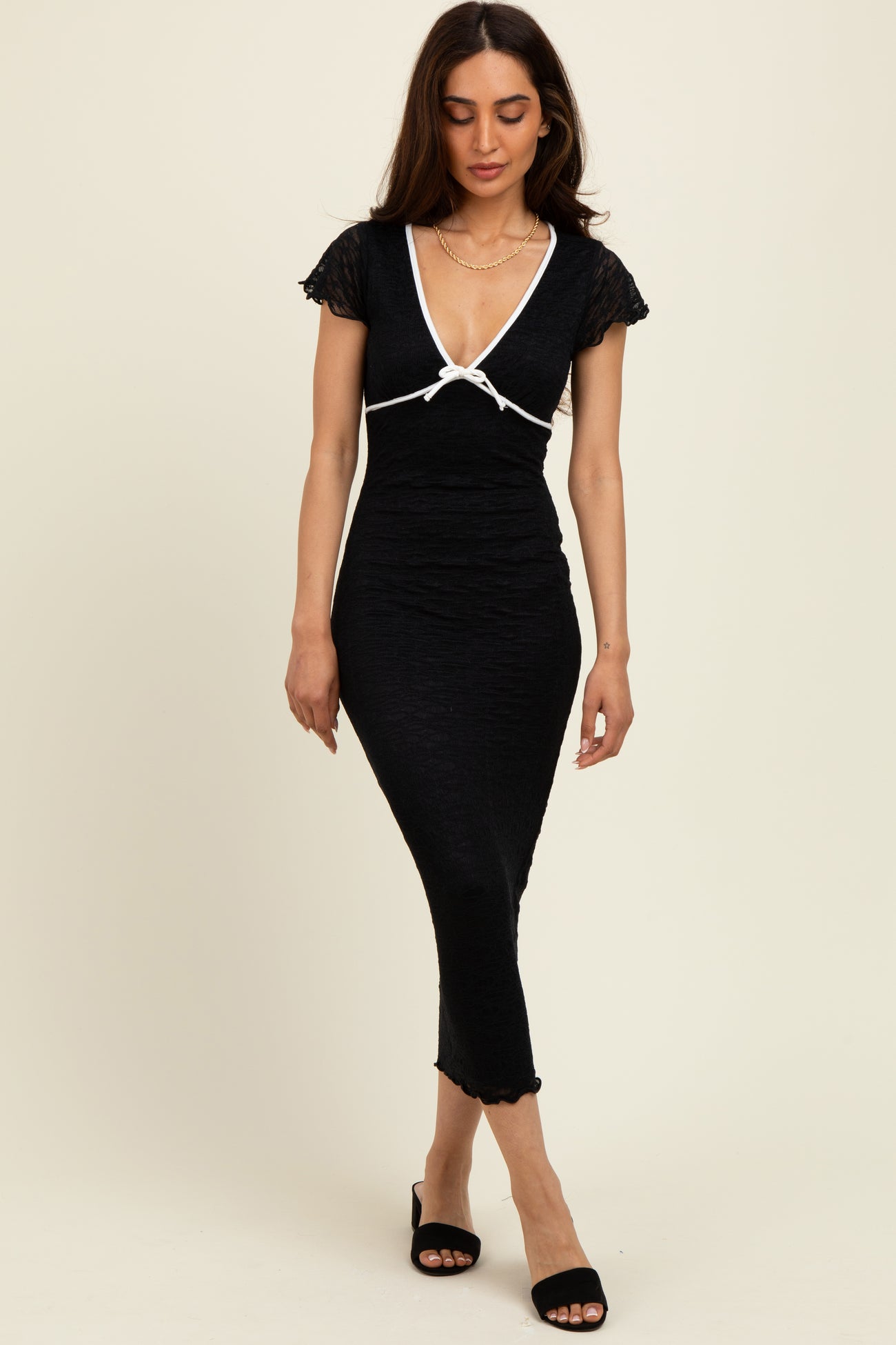 woman wearing a black fitted midi dress with short sleeves and white trim details, posing confidently