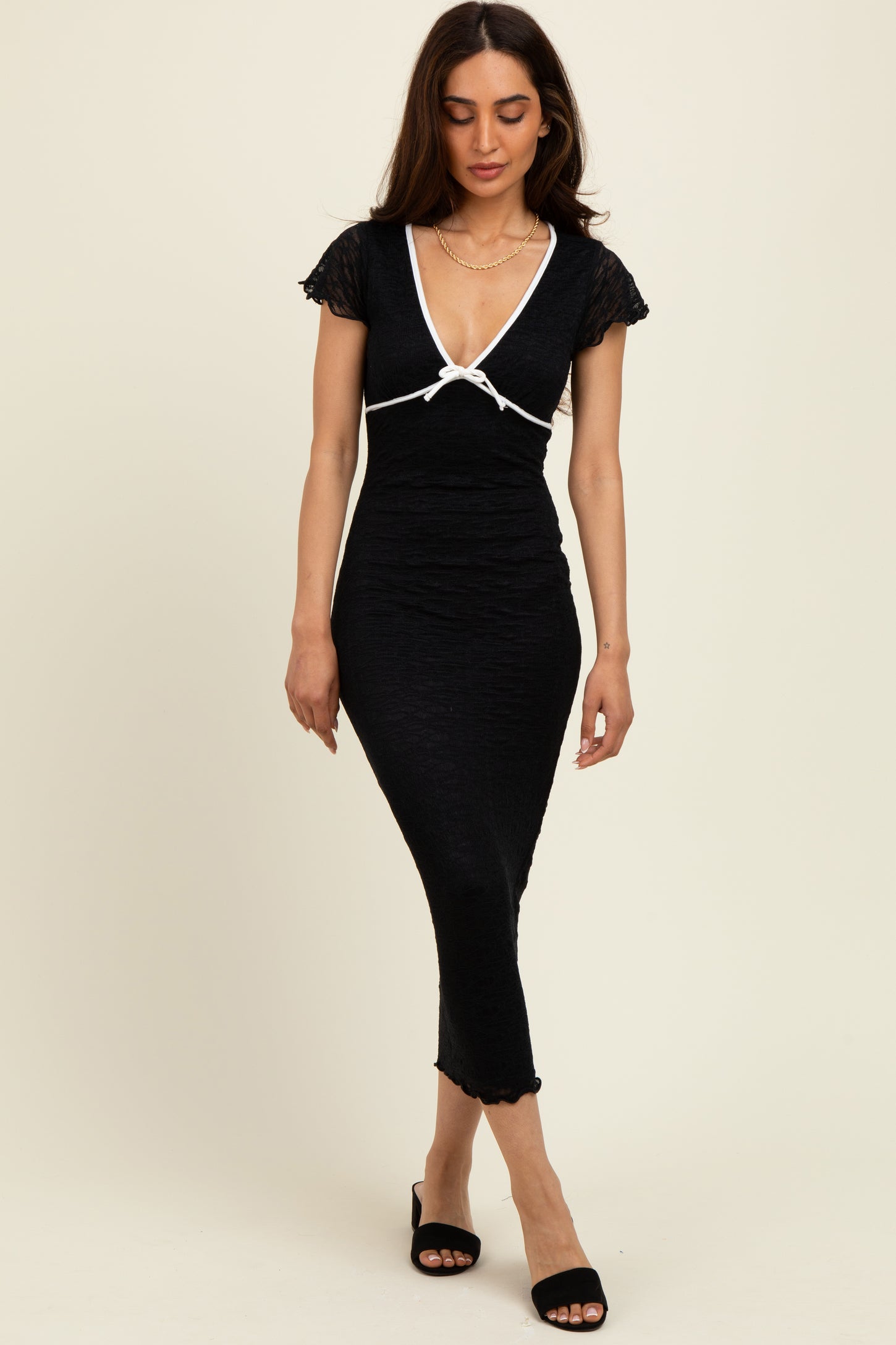 woman wearing a black fitted midi dress with short sleeves and white trim details, posing confidently