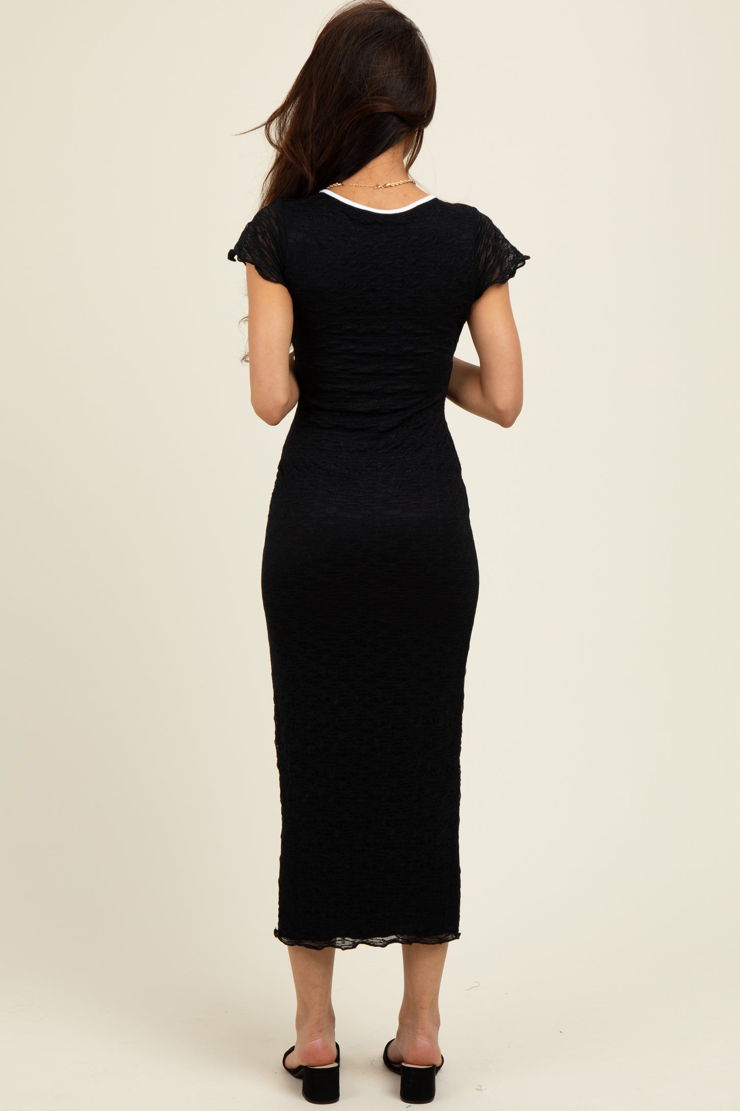 woman wearing a black midi dress with cap sleeves and a fitted silhouette, viewed from the back