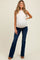 woman wearing a cream maternity tank top and dark blue flared jeans, with a visible baby bump