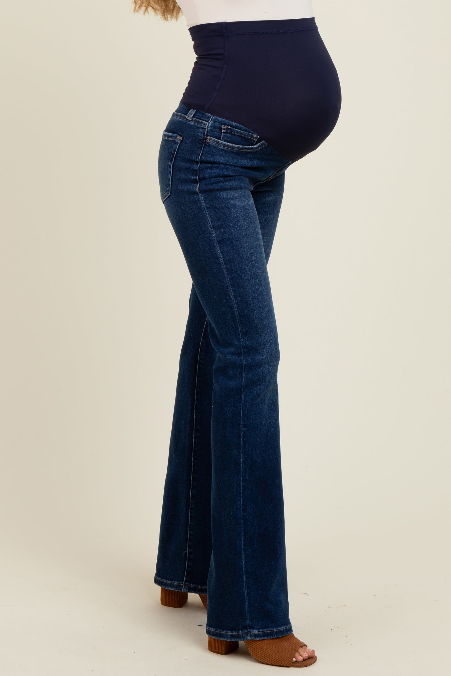 woman wearing dark blue maternity flared jeans with a belly panel, showing her baby bump