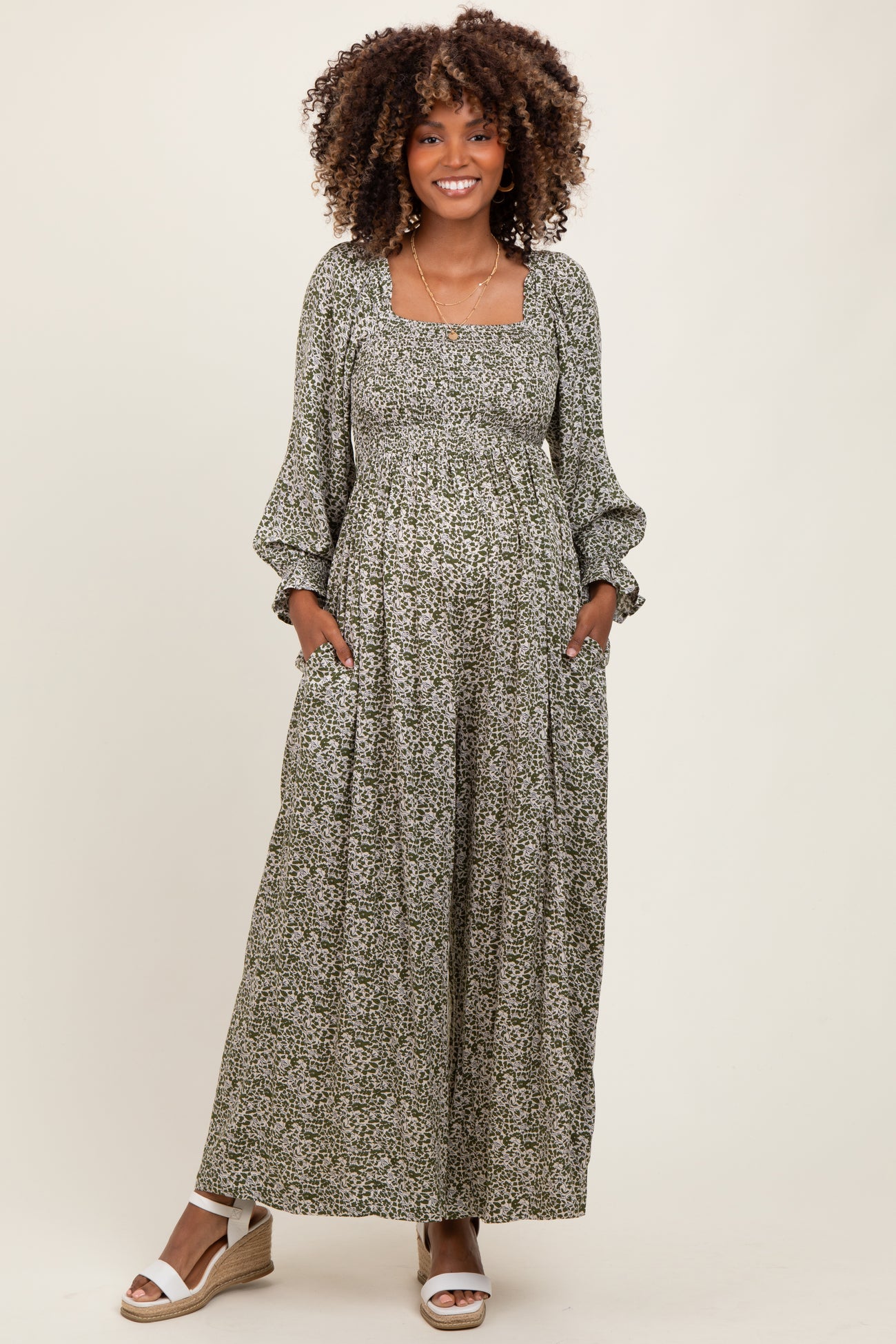 woman wearing a green floral maternity maxi dress with long sleeves and pockets, showing her baby bump