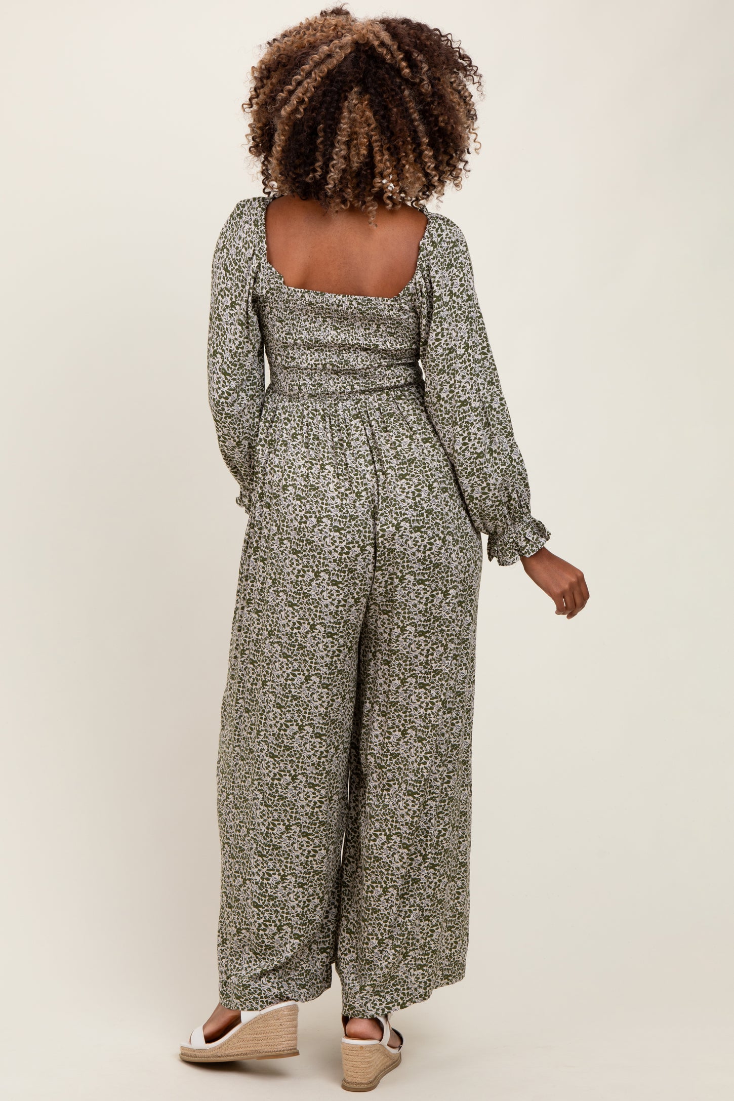woman wearing a floral print maternity jumpsuit with a smocked back and long sleeves, showing her baby bump from the side