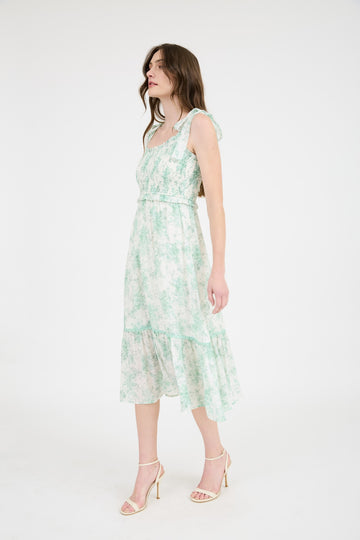 woman wearing a floral green and white midi dress with adjustable straps and a tiered skirt
