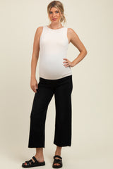 woman wearing a white sleeveless maternity top and black wide-leg jeans, showcasing her baby bump