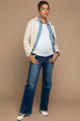 woman wearing a light beige quilted jacket, white maternity top, and flared jeans with a visible baby bump