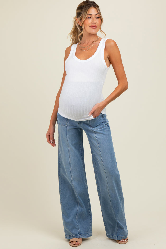 woman wearing a white maternity tank top and high-waisted blue wide-leg jeans, gently holding her baby bump