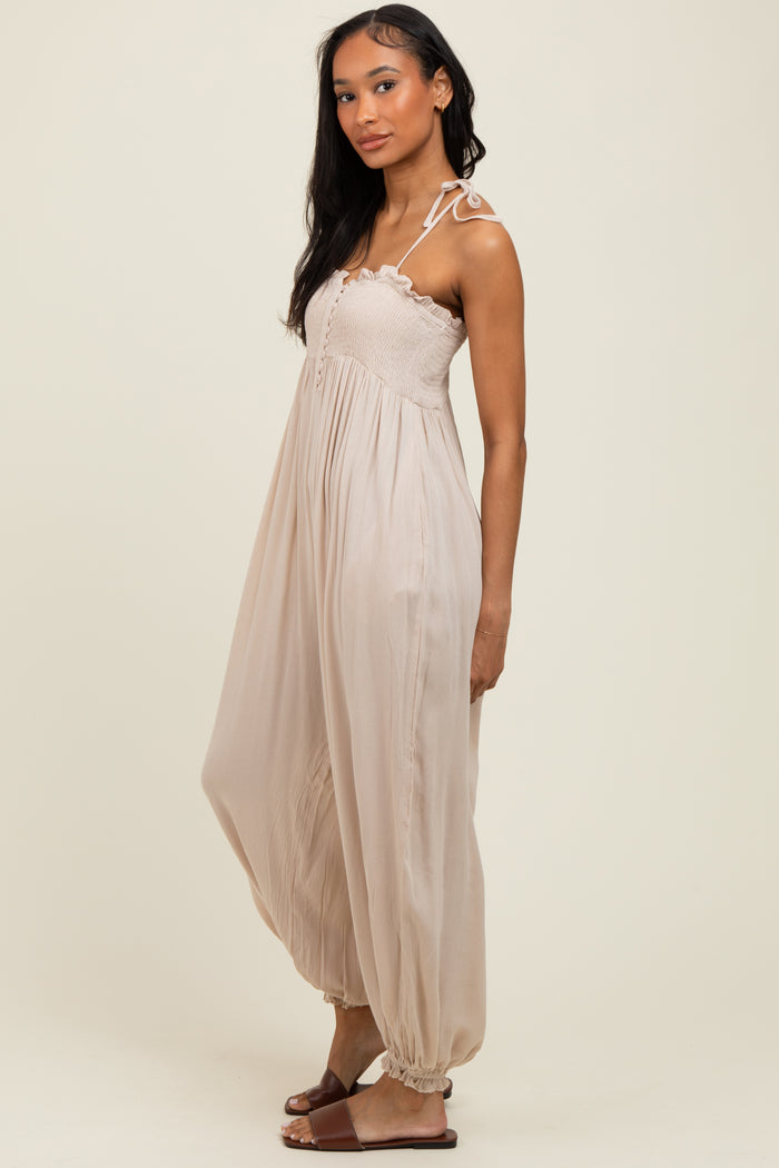 woman wearing a beige sleeveless maxi dress with a smocked bodice and tie straps, standing sideways