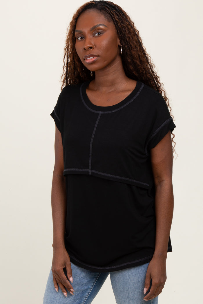 woman wearing a black short sleeve top with a scooped neckline and contrast stitching, paired with light blue jeans