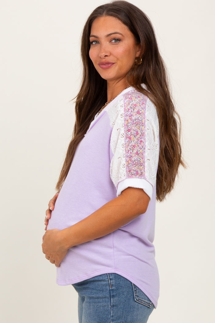 woman wearing a purple maternity top with lace floral sleeves and holding her baby bump