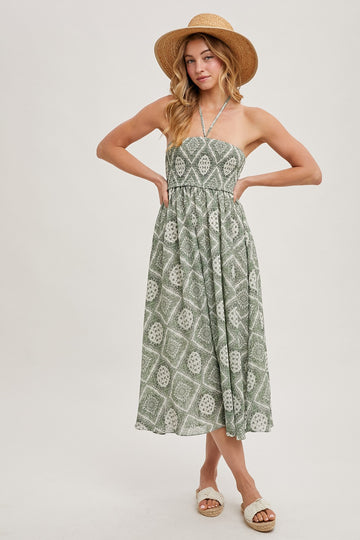 woman wearing a green patterned strapless midi dress and a straw hat, standing with hands on hips