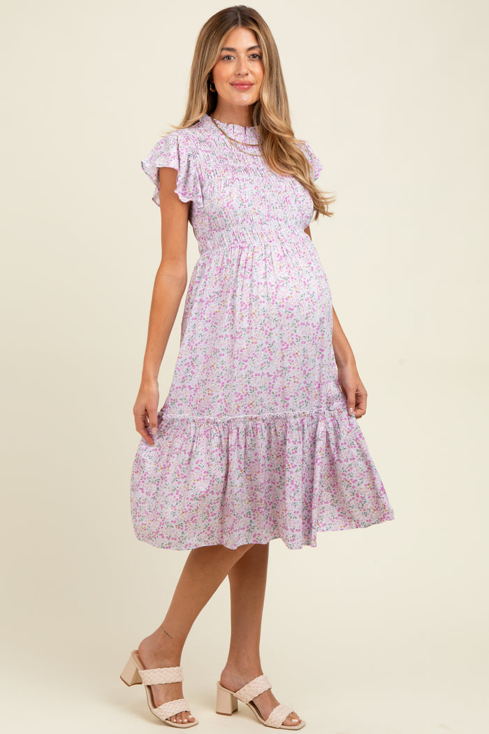 woman wearing a lilac floral maternity dress with short ruffled sleeves and a tiered skirt, showing her baby bump