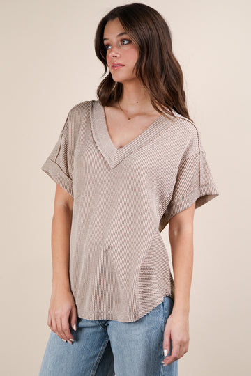 woman wearing a taupe oversized v-neck knit top with short sleeves and a relaxed fit paired with light blue jeans