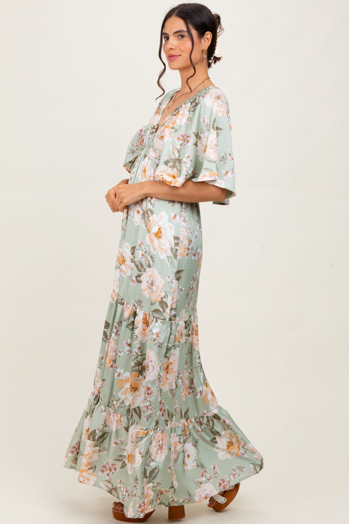 woman wearing a light green floral maxi dress with short flutter sleeves and a tiered skirt