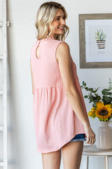 woman wearing a light pink sleeveless top with a keyhole back and ruffle detailing, styled with denim shorts