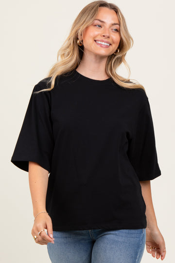 woman wearing a black oversized t-shirt and blue jeans, smiling against a light background