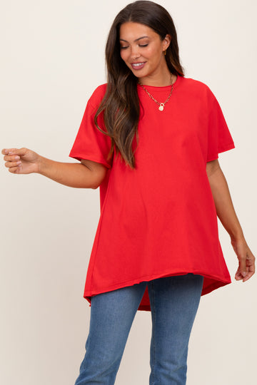woman wearing a red oversized maternity t-shirt with a rounded hem and a visible baby bump, paired with blue jeans