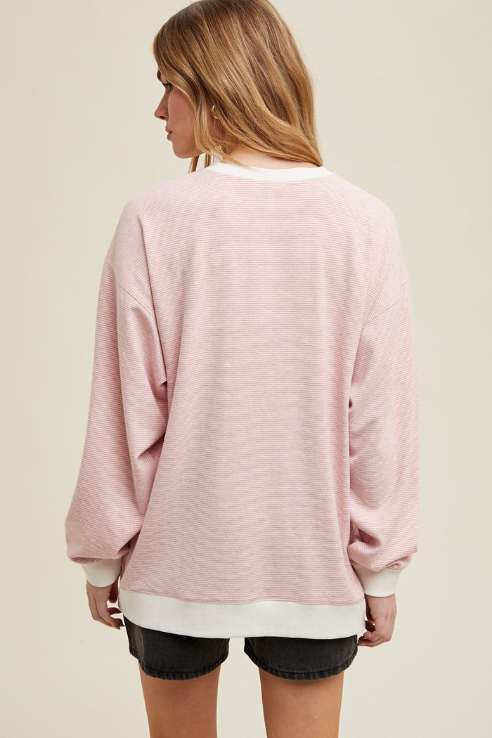 woman wearing a pink oversized sweatshirt with white trim and long sleeves, view from the back