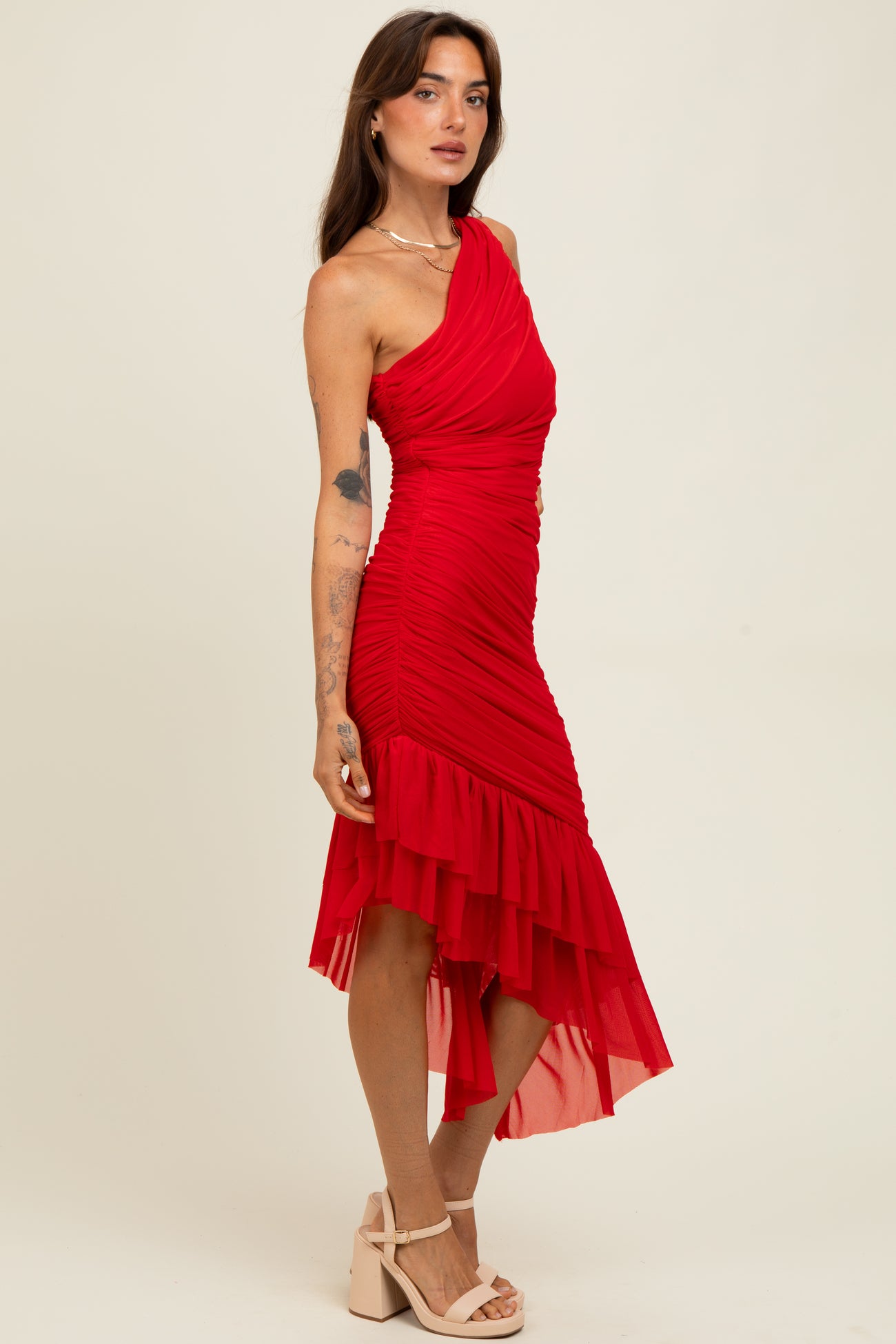 woman wearing a red one-shoulder dress with ruching and a layered hemline, standing on a beige background