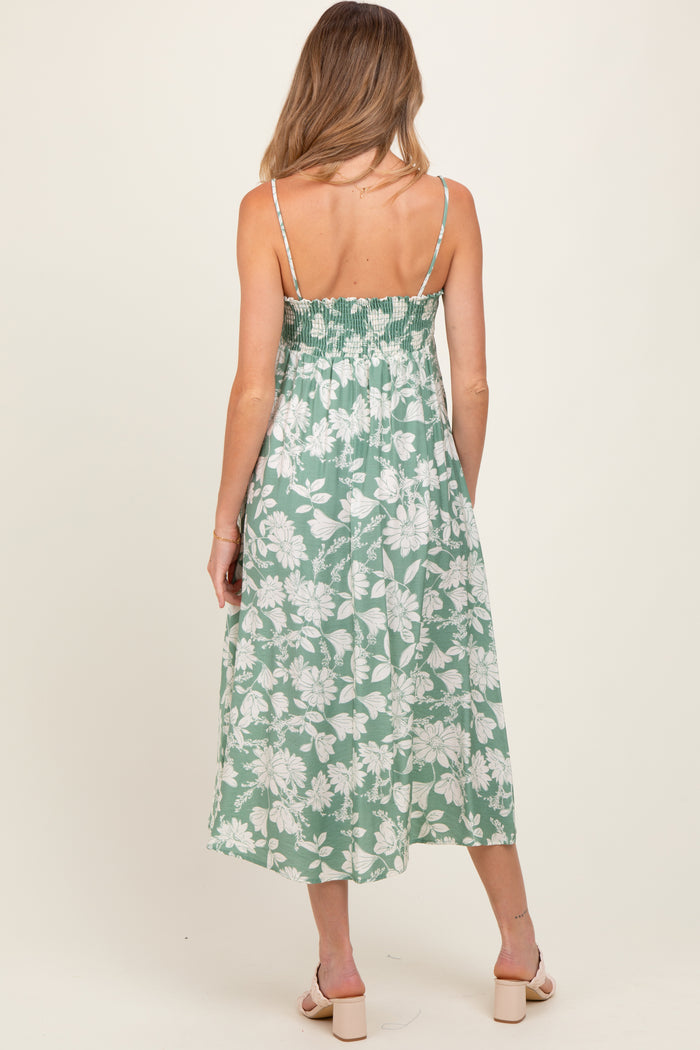 woman wearing a green floral maternity dress with smocked back and spaghetti straps, showing her baby bump