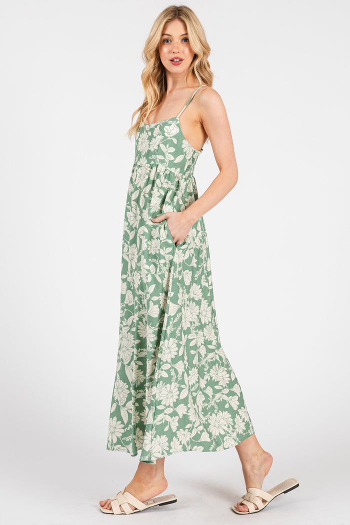 woman wearing a green floral maxi dress with adjustable straps and pockets, styled with beige slide sandals
