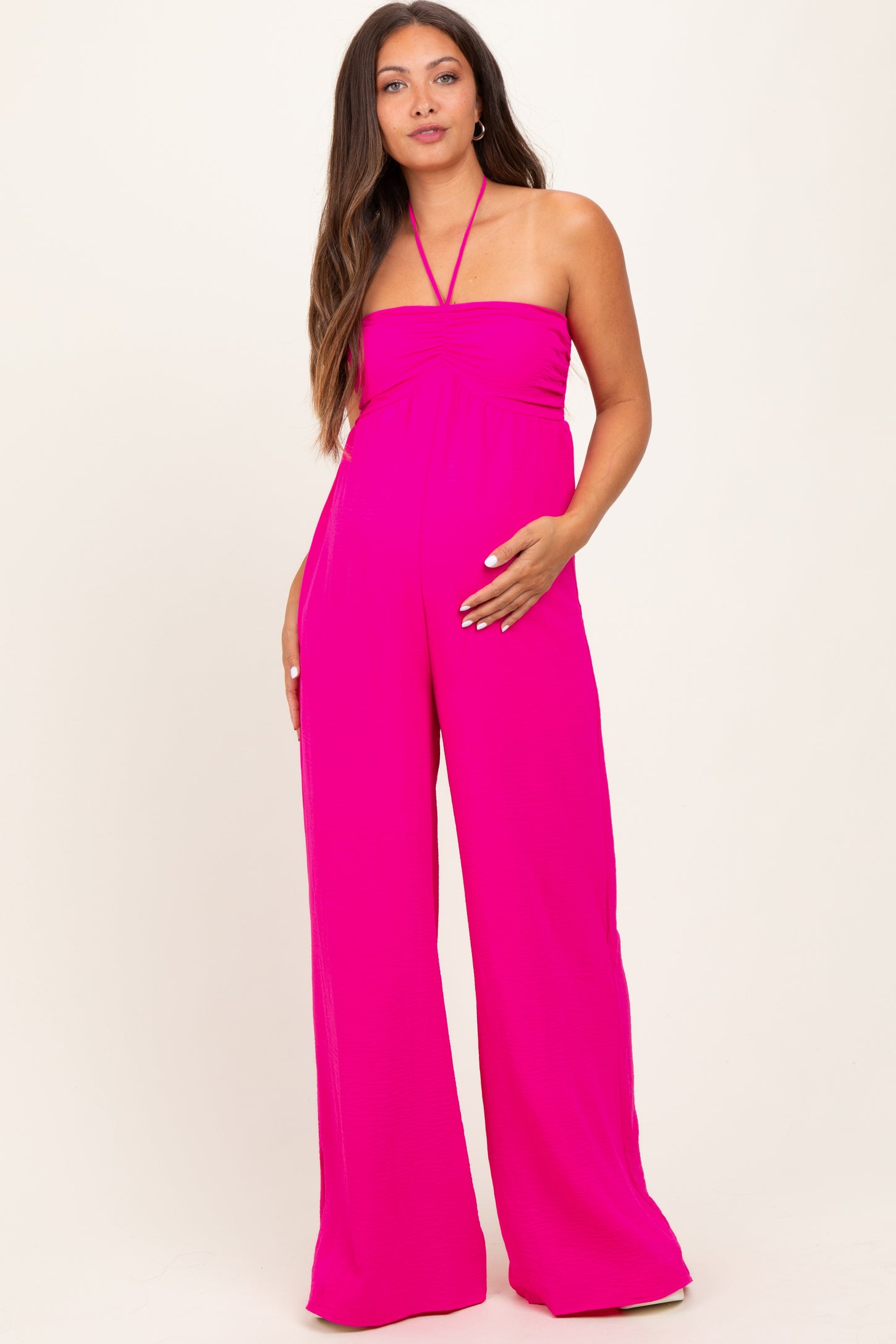 woman wearing a bright pink strapless maternity jumpsuit and holding her baby bump