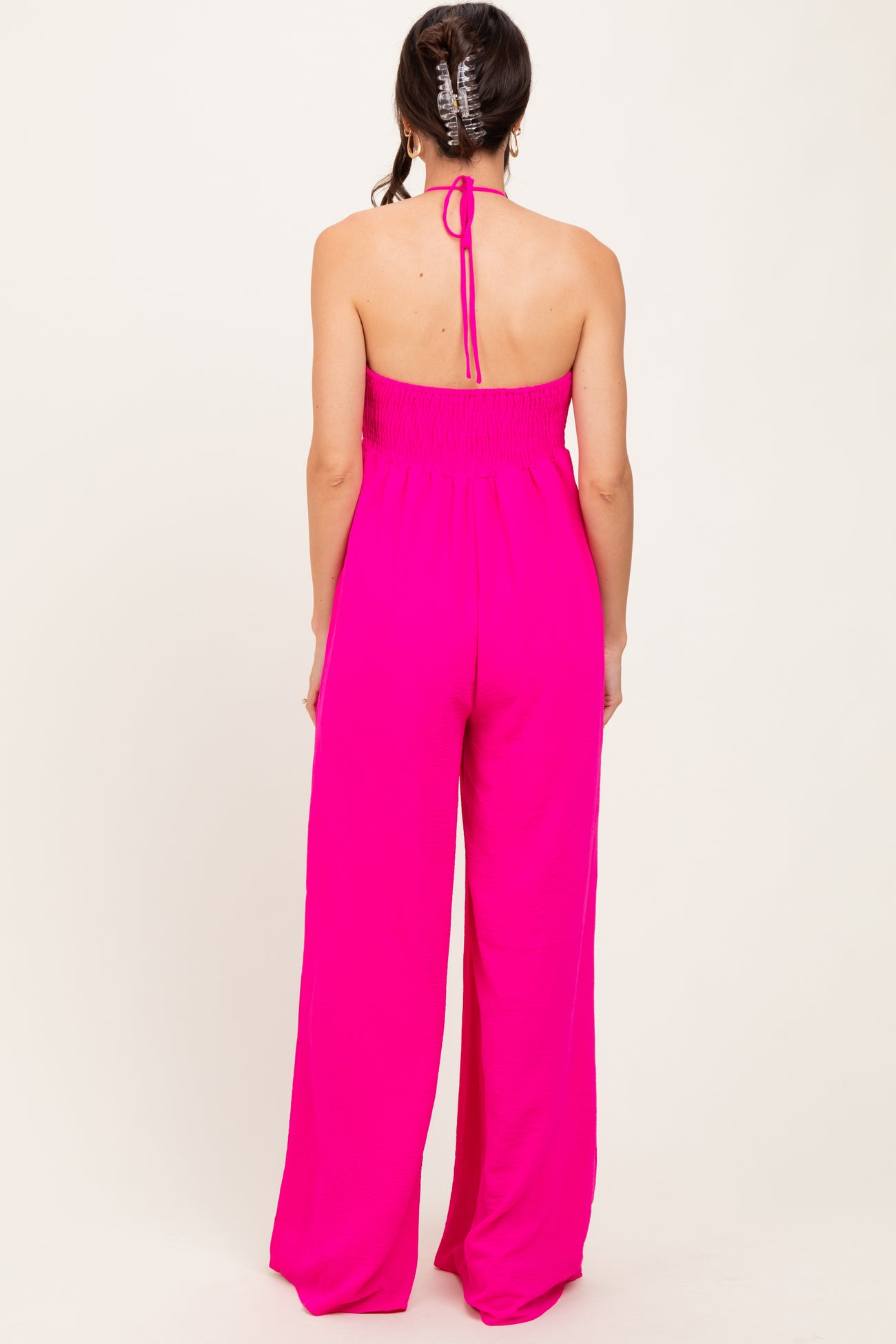 woman wearing a bright pink halter neck jumpsuit with a smocked bodice and wide leg pants seen from the back