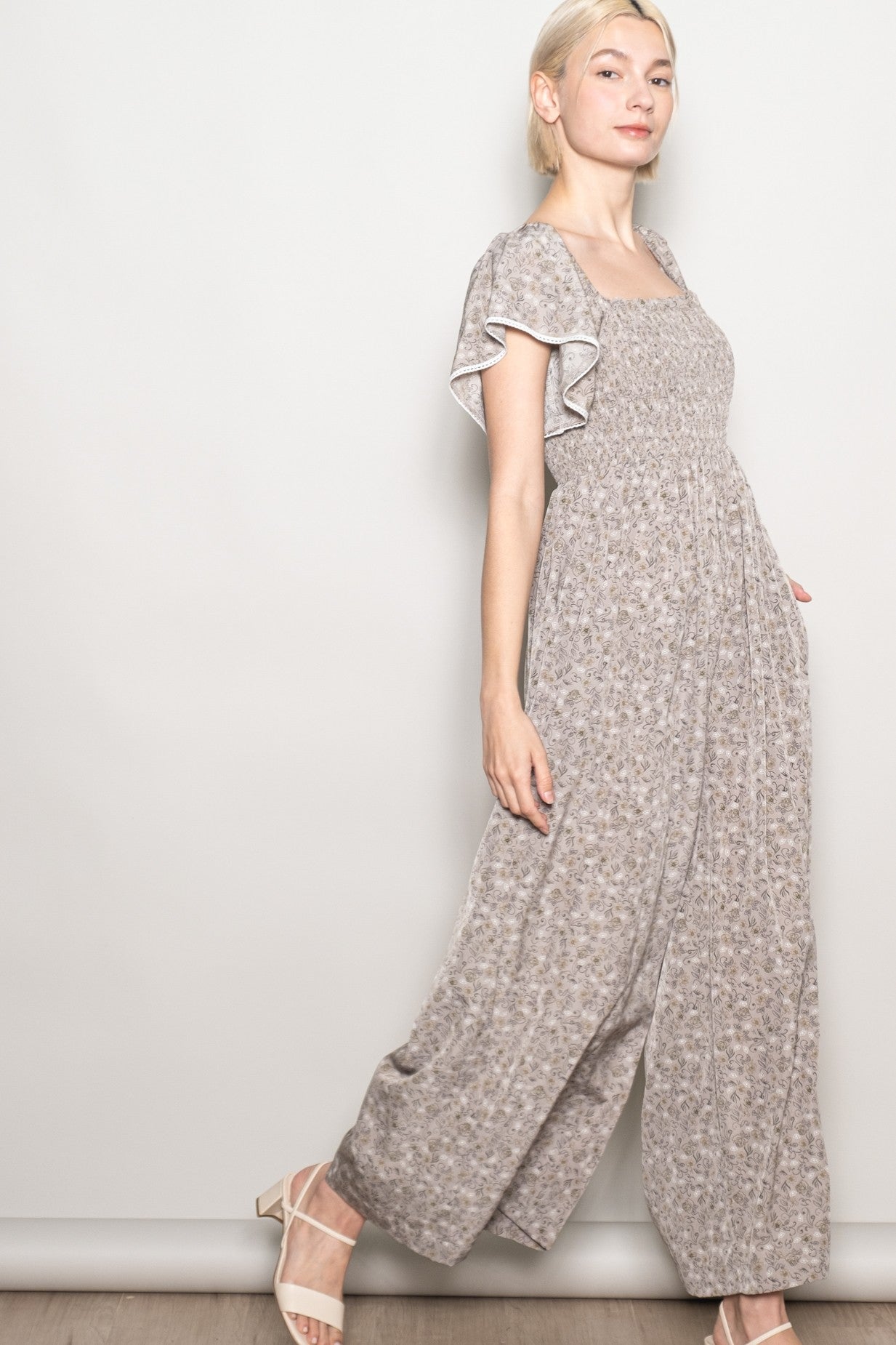 woman wearing a light brown floral jumpsuit with ruffled sleeves and wide leg fit