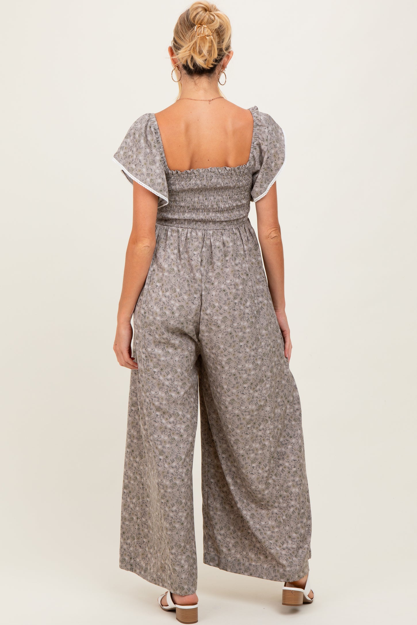 woman wearing a gray floral maternity jumpsuit with puff sleeves, styled in a relaxed fit from the back