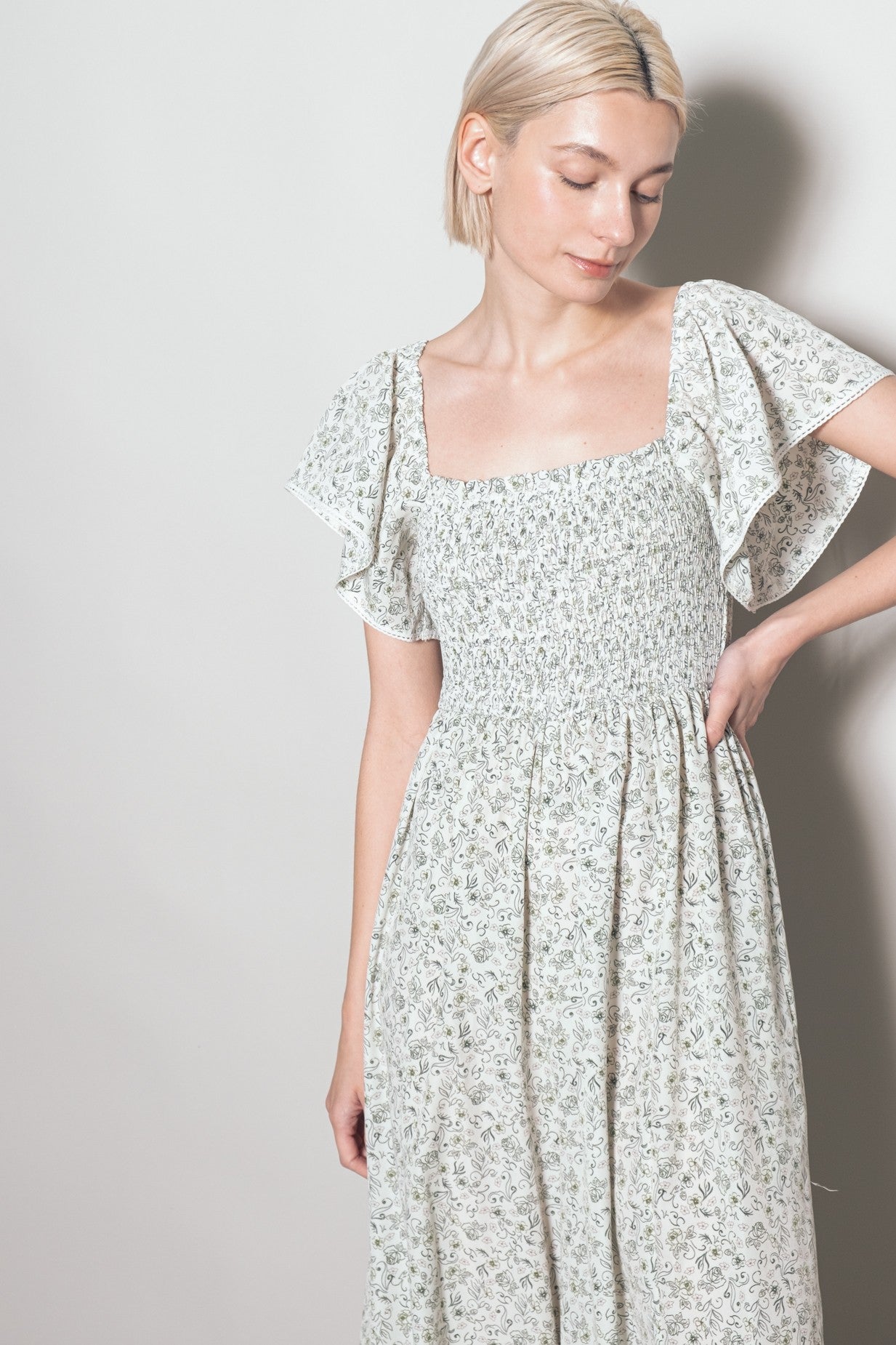 woman wearing a light floral smocked midi dress with flutter sleeves and a square neckline