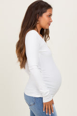 woman wearing a white long sleeve maternity top and showing her baby bump while standing sideways