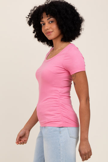 woman wearing a fitted pink ribbed short sleeve top and light blue jeans, smiling and posing sideways