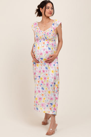 woman wearing a floral maternity maxi dress with ruffled straps, cradling her baby bump