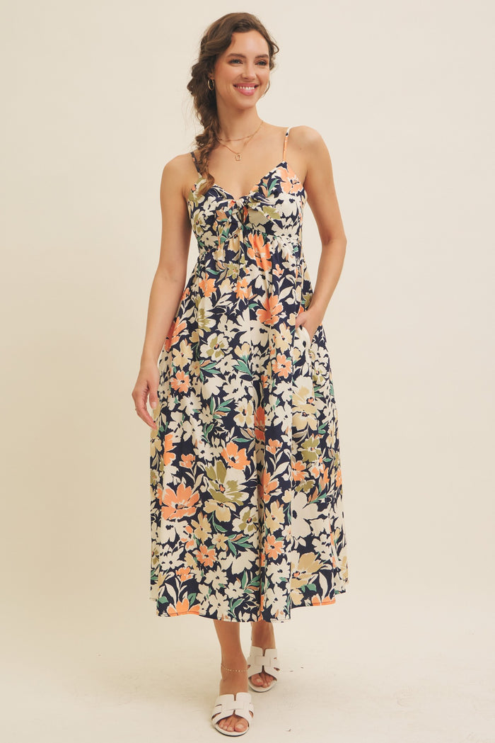 woman wearing a floral midi dress with a sweetheart neckline and adjustable straps, standing with hands in pockets
