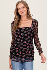 woman wearing a black sheer long sleeve top with floral print and ruched detailing, styled with blue jeans