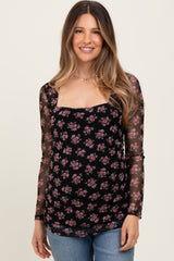 woman wearing a black floral maternity top with sheer long sleeves and a visible baby bump