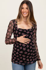 woman wearing a black floral maternity top with long sheer sleeves and a visible baby bump