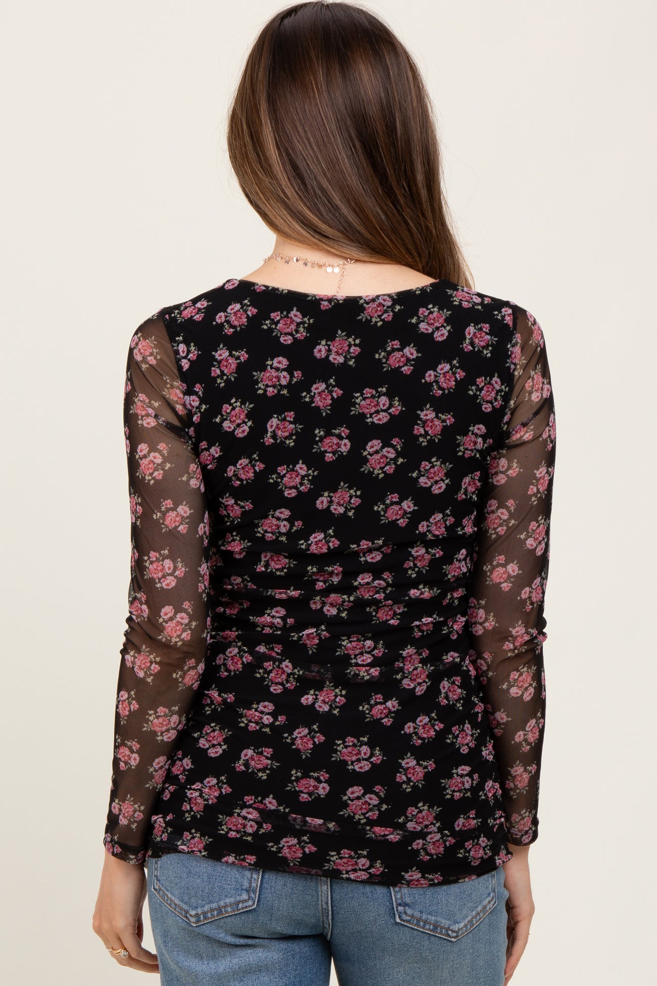 woman wearing a black floral maternity top with sheer long sleeves, viewed from the back