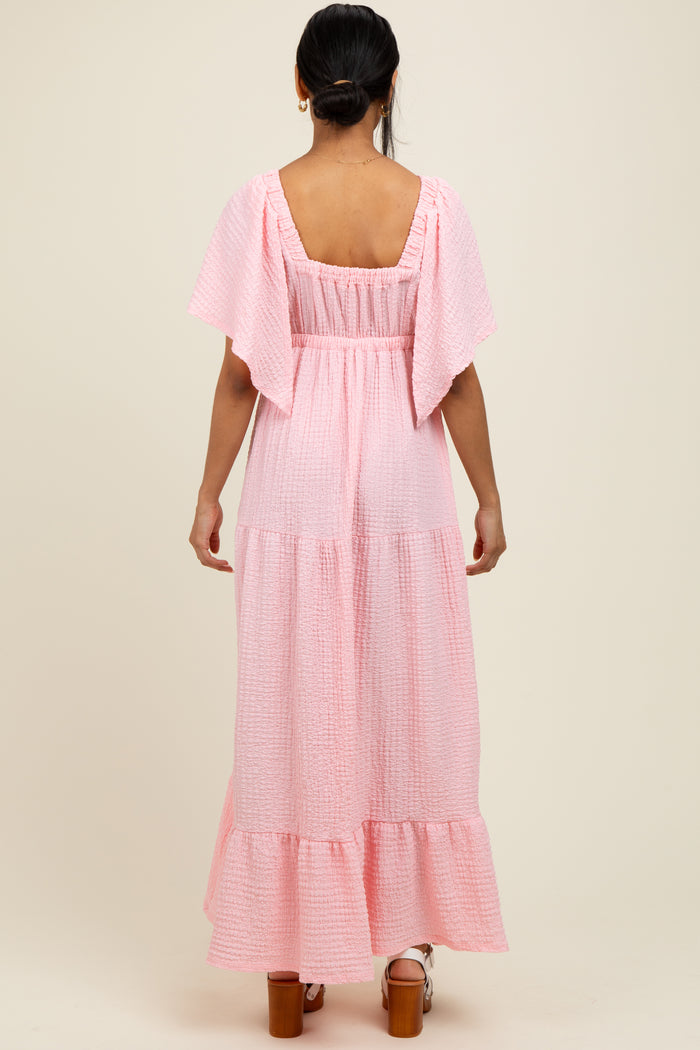 woman wearing a pink tiered maxi dress with flutter sleeves and a smocked back detail